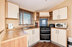 A compact kitchen with a stove, microwave, and a window with blinds.