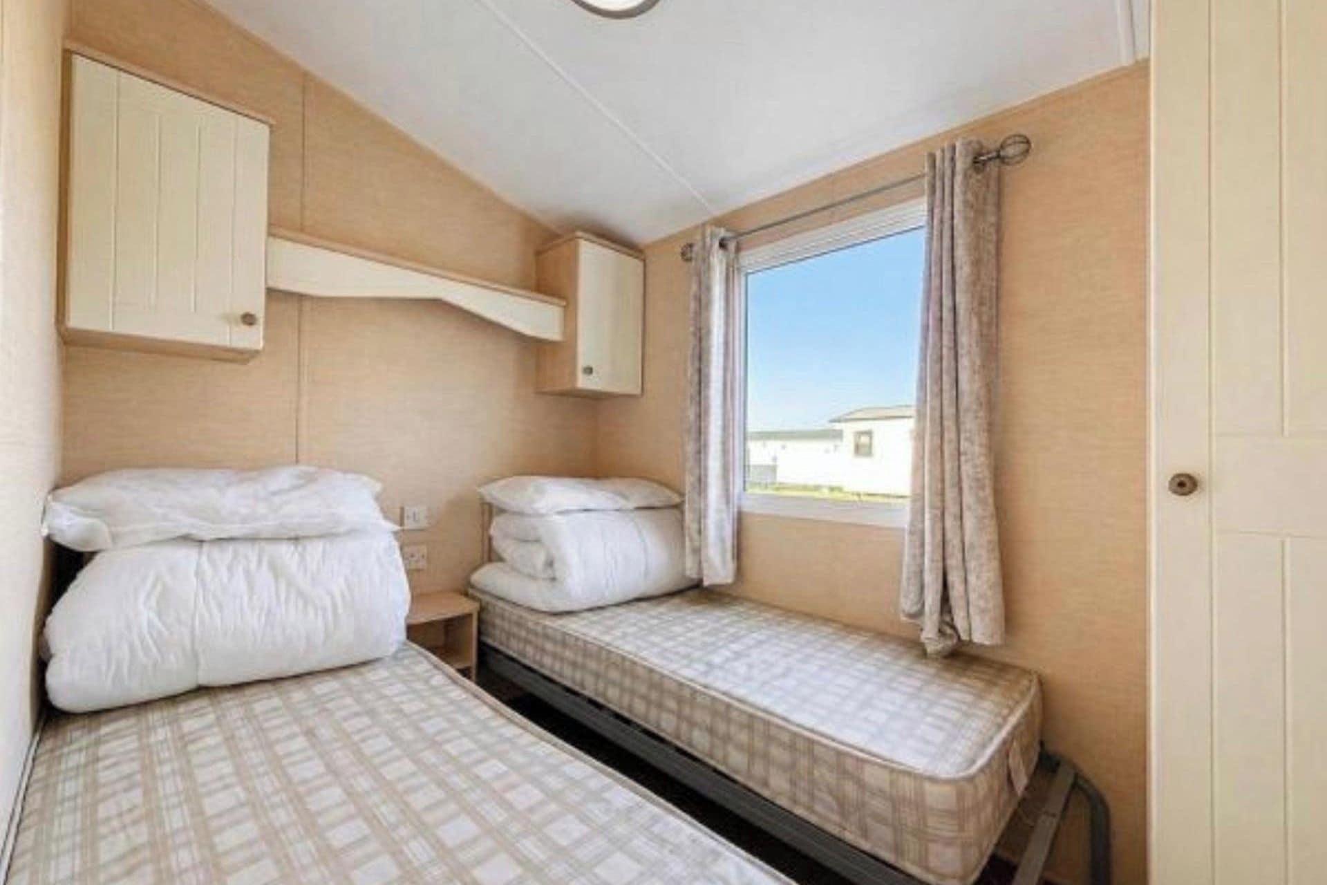 Una habitación pequeña y funcional con dos camas, una ventana con cortinas y un armario de madera.
