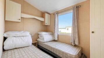 Una habitación pequeña y funcional con dos camas, una ventana con cortinas y un armario de madera.