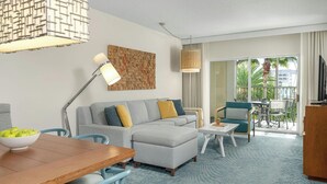 Ein modernes Wohnzimmer mit einer Couch, einem Esstisch mit Stühlen, einem Fernseher und einem Balkon mit Blick auf Palmen.