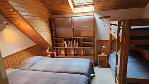 Een gezellige kamer met twee bedden, een houten boekenkast en een dakvenster.