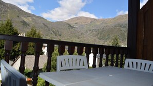 Een balkon met een tafel en stoelen, met uitzicht op een bergachtig landschap.