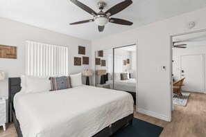 A bedroom with a bed, bedside tables, a ceiling fan, and a mirror. - New Walkable PB Living | 1-Bed Parking Included (San Diego)