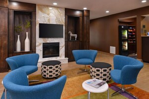 A modern lounge area with blue armchairs, a fireplace, a flat-screen TV, and a vending machine.