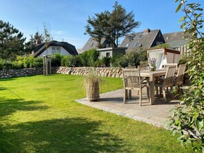 Un pati ben cuidat amb una paret de pedra, un prat verd i una zona de dinar amb mobles de fusta.