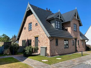 Ein zweistöckiges Backsteinhaus mit einem steilen Satteldach, einer Haustür und einem kleinen Vorgarten mit einem Weg.