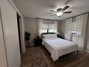 A bedroom with a bed, nightstands, a ceiling fan, and a window with curtains.