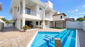 Ein modernes, zweistöckiges Haus mit Swimmingpool, überdachter Terrasse und einem umzäunten Garten.