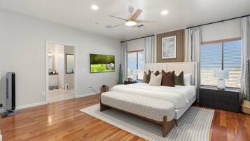 A bedroom with a bed, a ceiling fan, a TV, and a window with curtains.