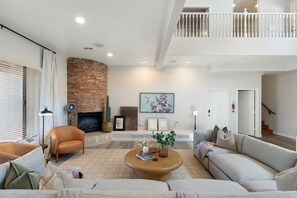 Ein geräumiges Wohnzimmer mit Kamin, hohen Decken und einer Treppe zu einer oberen Ebene.