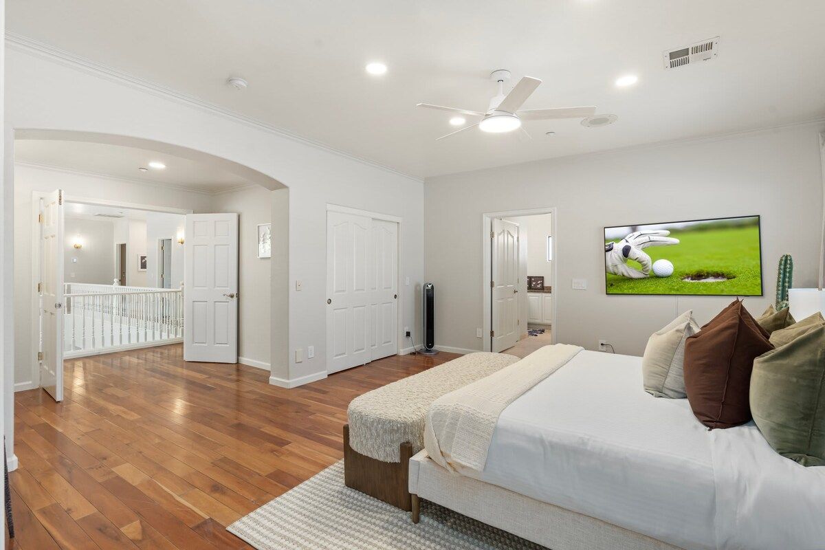 A bedroom with a bed, pillows, a television, and a ceiling fan.