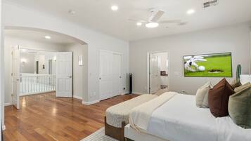 A bedroom with a bed, pillows, a television, and a ceiling fan.