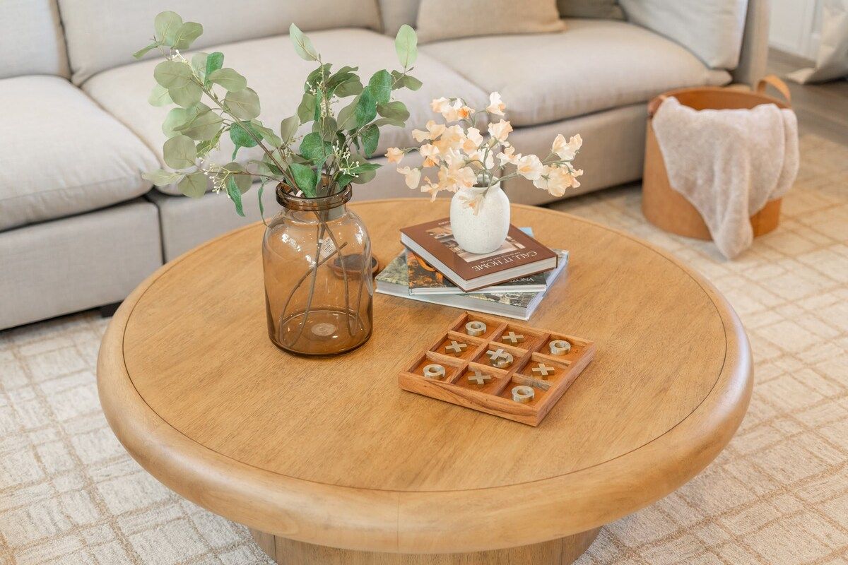 A round wooden coffee table with a glass vase, a book, and a wooden game board.