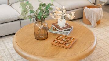 A round wooden coffee table with a glass vase, a book, and a wooden game board.