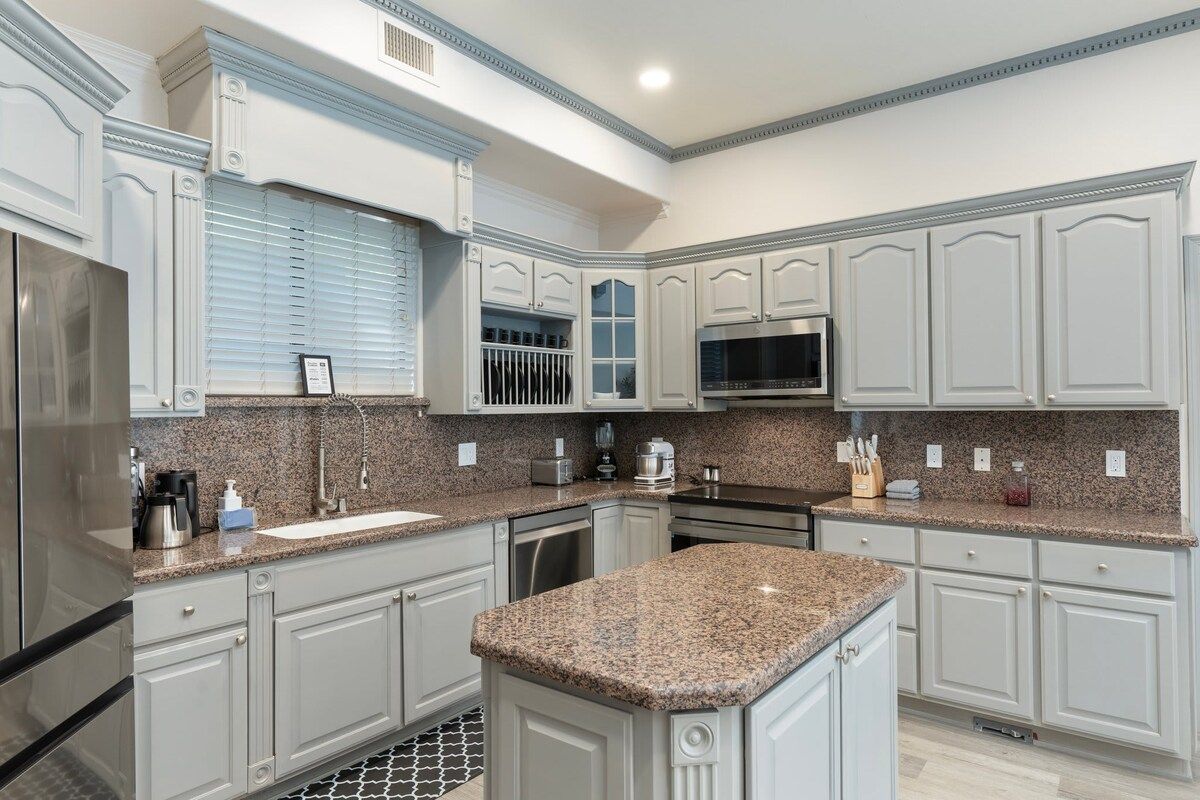 A kitchen with white cabinetry, granite countertops, a stainless steel refrigerator, and a microwave.
