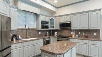 A kitchen with white cabinetry, granite countertops, a stainless steel refrigerator, and a microwave.