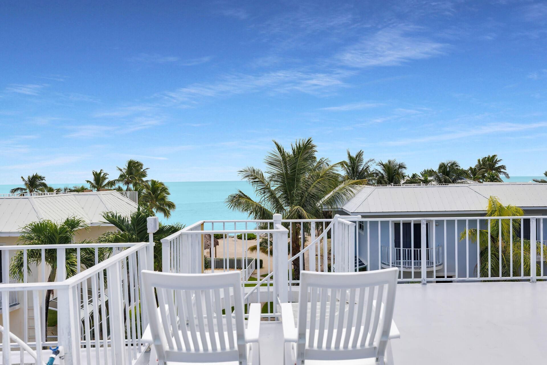 A balcony with white chairs and a view of the ocean.