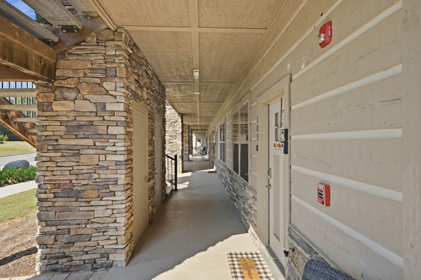 A covered corridor with stone walls, doors, and a fire alarm.