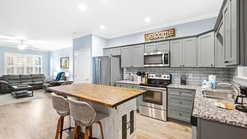 Une cuisine moderne avec des meubles gris, un îlot central en bois doté de tabourets, un four en acier inoxydable et un four à micro-ondes.