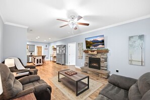 A spacious living room with a fireplace, a ceiling fan, and a kitchen in the background.