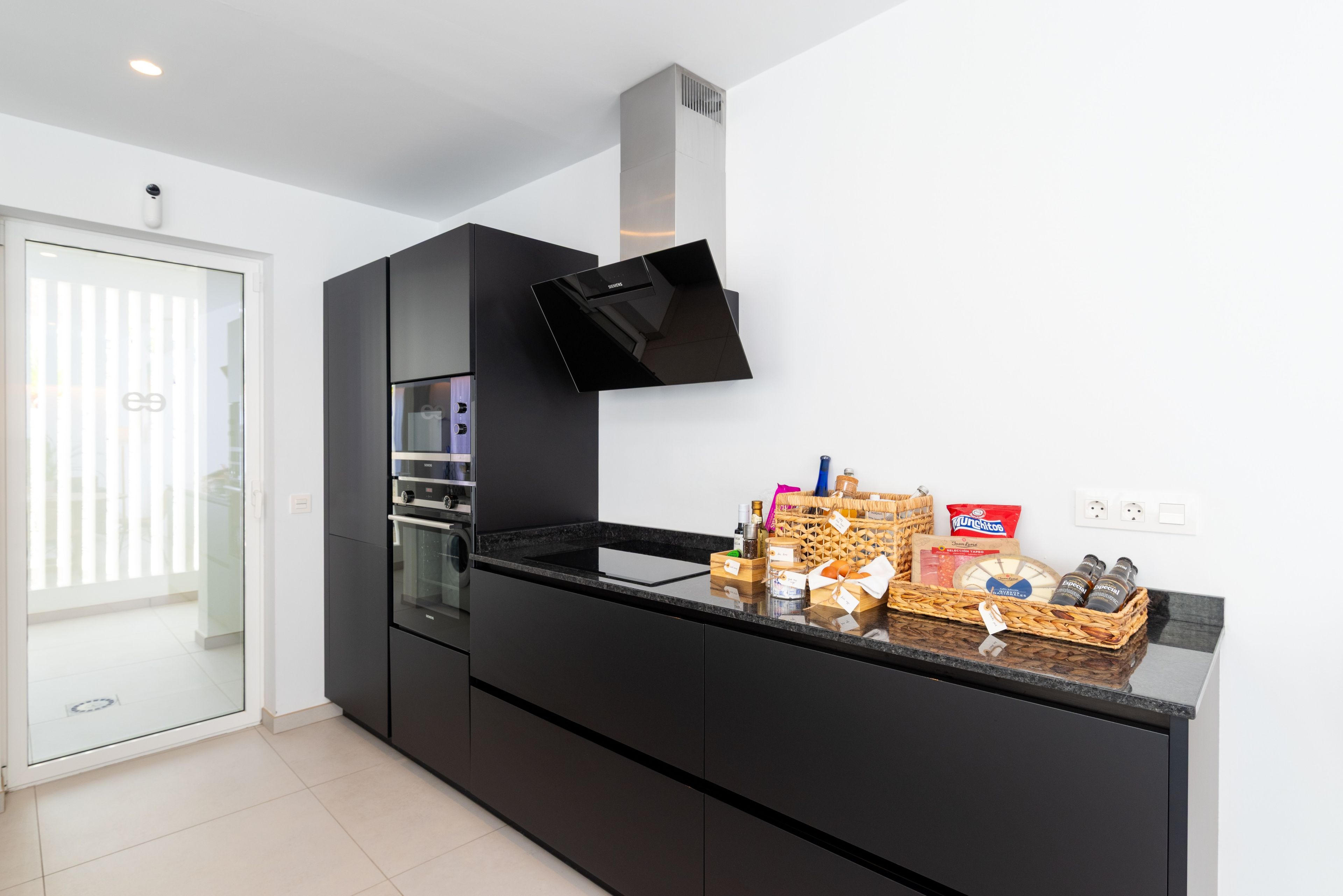 Une cuisine moderne avec des meubles de rangement noirs, un four encastré et un plan de travail sur lequel on trouve divers aliments et condiments.