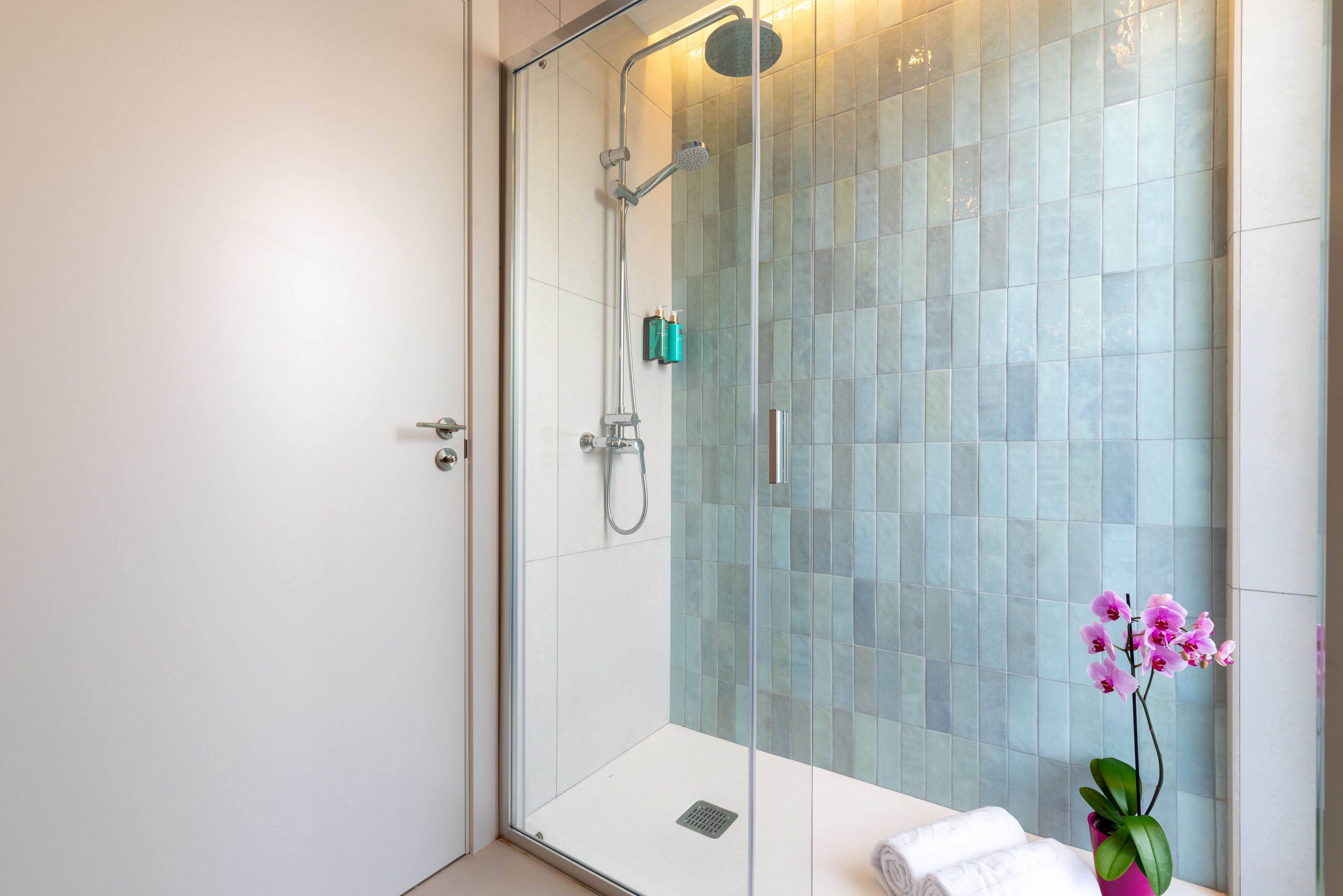 A modern bathroom with a glass-enclosed shower, a white sink, and a pink orchid.