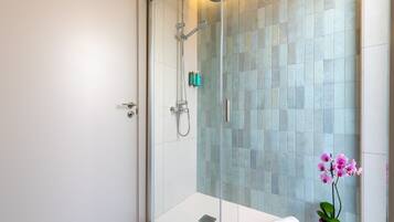 A modern bathroom with a glass-enclosed shower, a white sink, and a pink orchid.