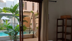 Quarto com cama grande, mesa de cabeceira de madeira e vista para piscina e área externa.