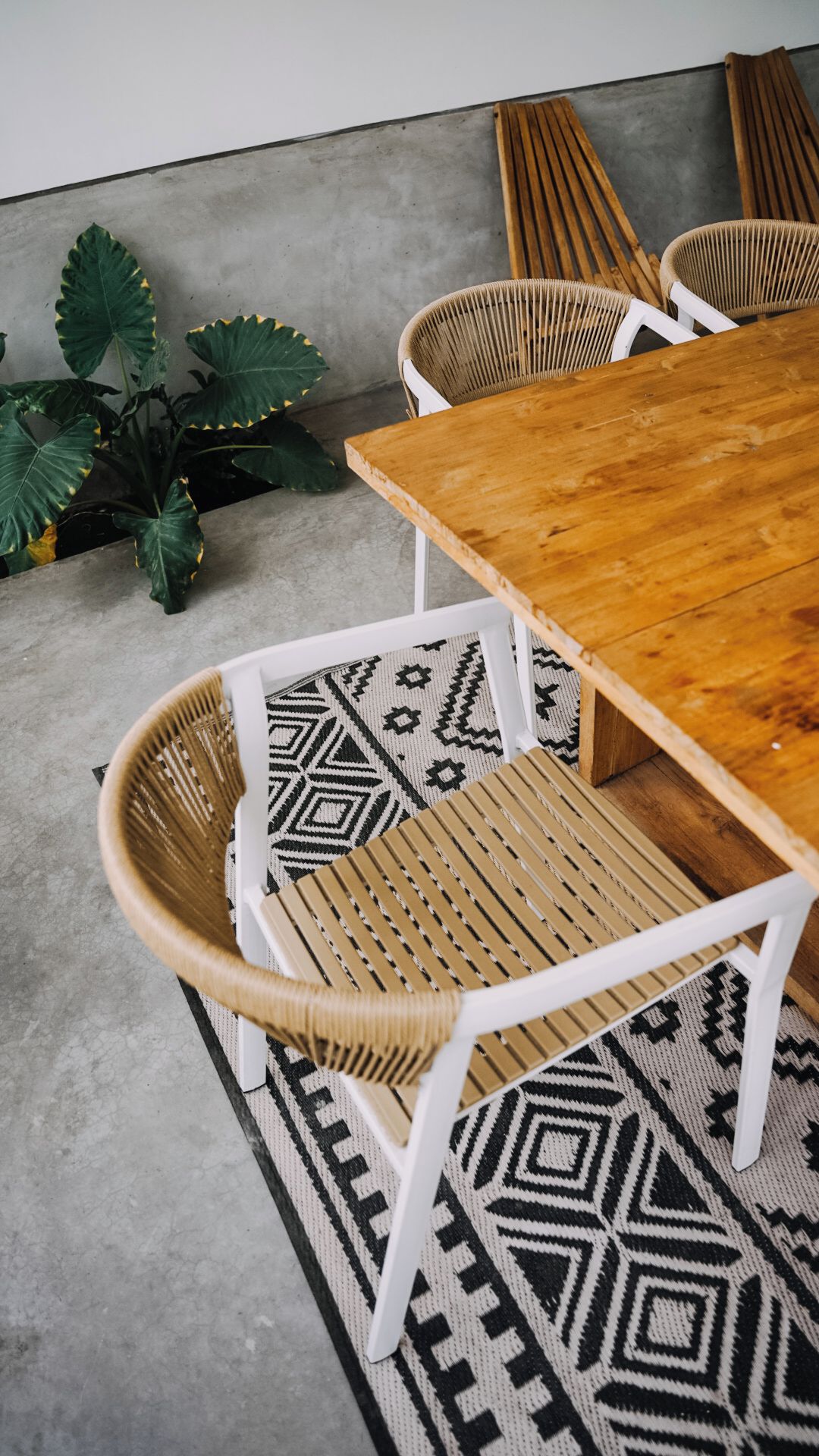 A wooden dining table with woven chairs and a patterned rug.