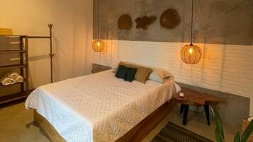 A bedroom with a bed, bedside table, hanging light fixture, and a potted plant.