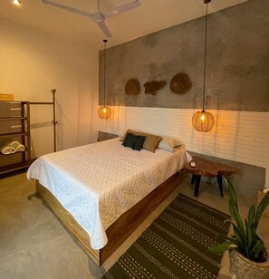 Un dormitorio con cama, mesita de noche, lámpara colgante y una planta en maceta.