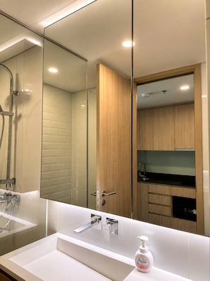 Een moderne badkamer met een grote spiegel, een douche en een wastafel met zeepdispenser.
