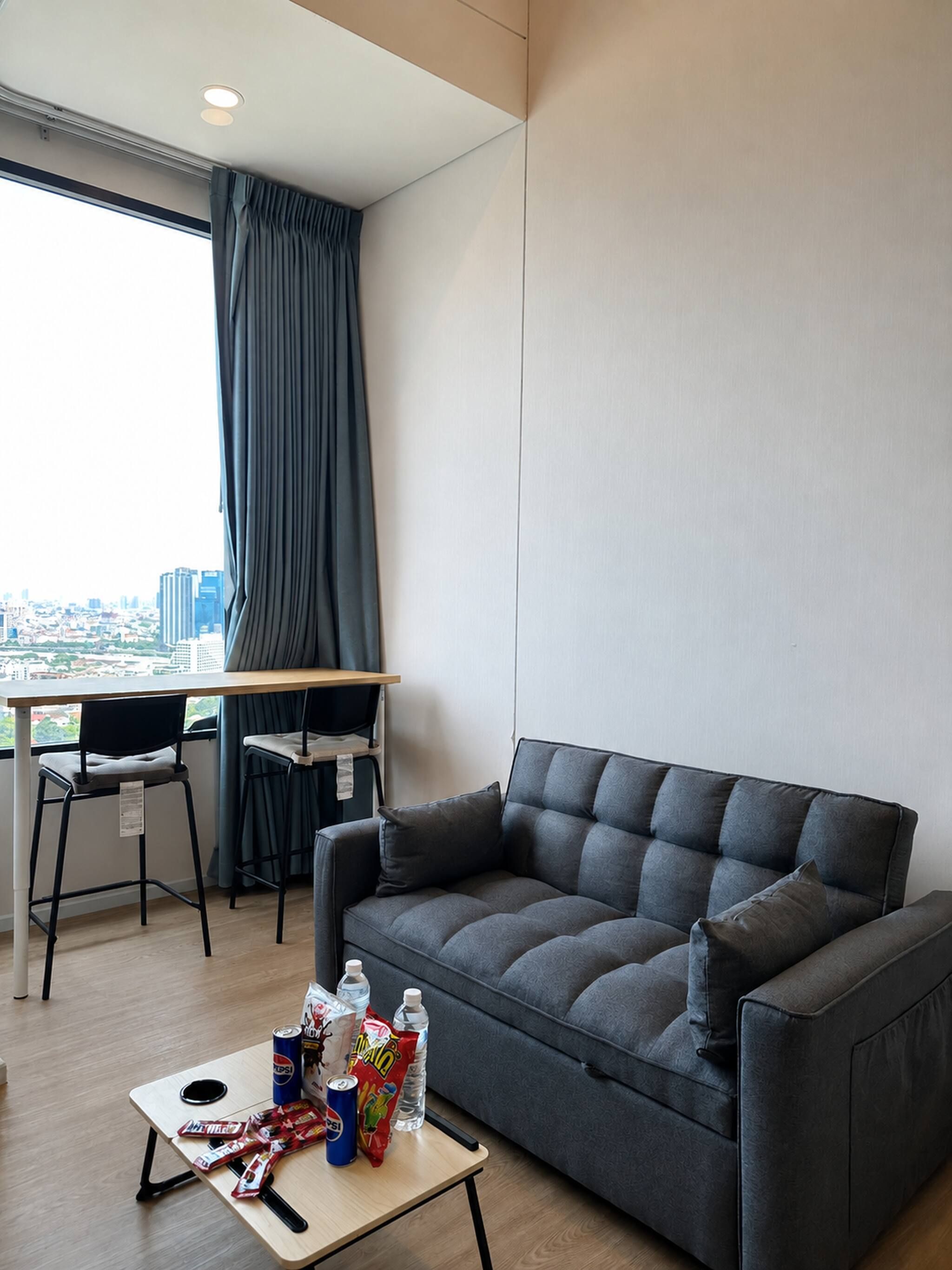 A modern living room with a grey sofa, a small table with snacks, and a desk with a chair.