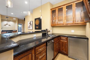A kitchen with wooden cabinets, a stainless steel refrigerator, and a black countertop. - Luxury 5BR Retreat, Heated Pool, Spa, Sport Court, Putting Green & Game Rooms (Scottsdale)