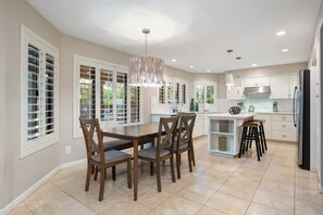A modern kitchen with white cabinetry, a dining area with wooden chairs, and a pendant light. - Luxury 5BR Retreat, Heated Pool, Spa, Sport Court, Putting Green & Game Rooms (Scottsdale)