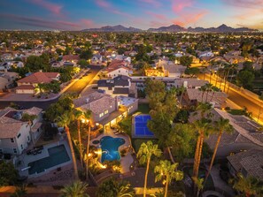 An aerial view of a residential area with houses, a swimming pool, and a mountain range in the background. - Luxury 5BR Retreat, Heated Pool, Spa, Sport Court, Putting Green & Game Rooms (Scottsdale)