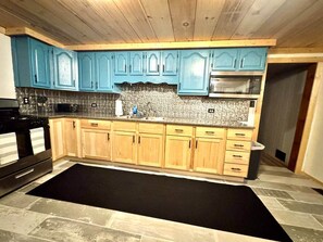 A kitchen with blue cabinets, a black rug, and a stone backsplash. - Trail Access Getaway Near Lake Saint Helen (St. Helen)