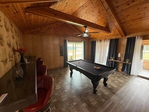 A pool table in a room with wooden walls and ceiling, a red chair, and a small table with a vase. - Trail Access Getaway Near Lake Saint Helen (St. Helen)