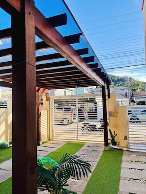A covered outdoor area with a metal gate, a paved pathway, and a small garden with artificial grass and a potted plant.