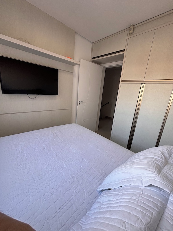 A hotel room with a bed, a television mounted on the wall, and a wardrobe.