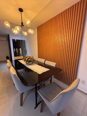 A modern dining area with a black table, grey upholstered chairs, a wooden accent wall, and a pendant light fixture.