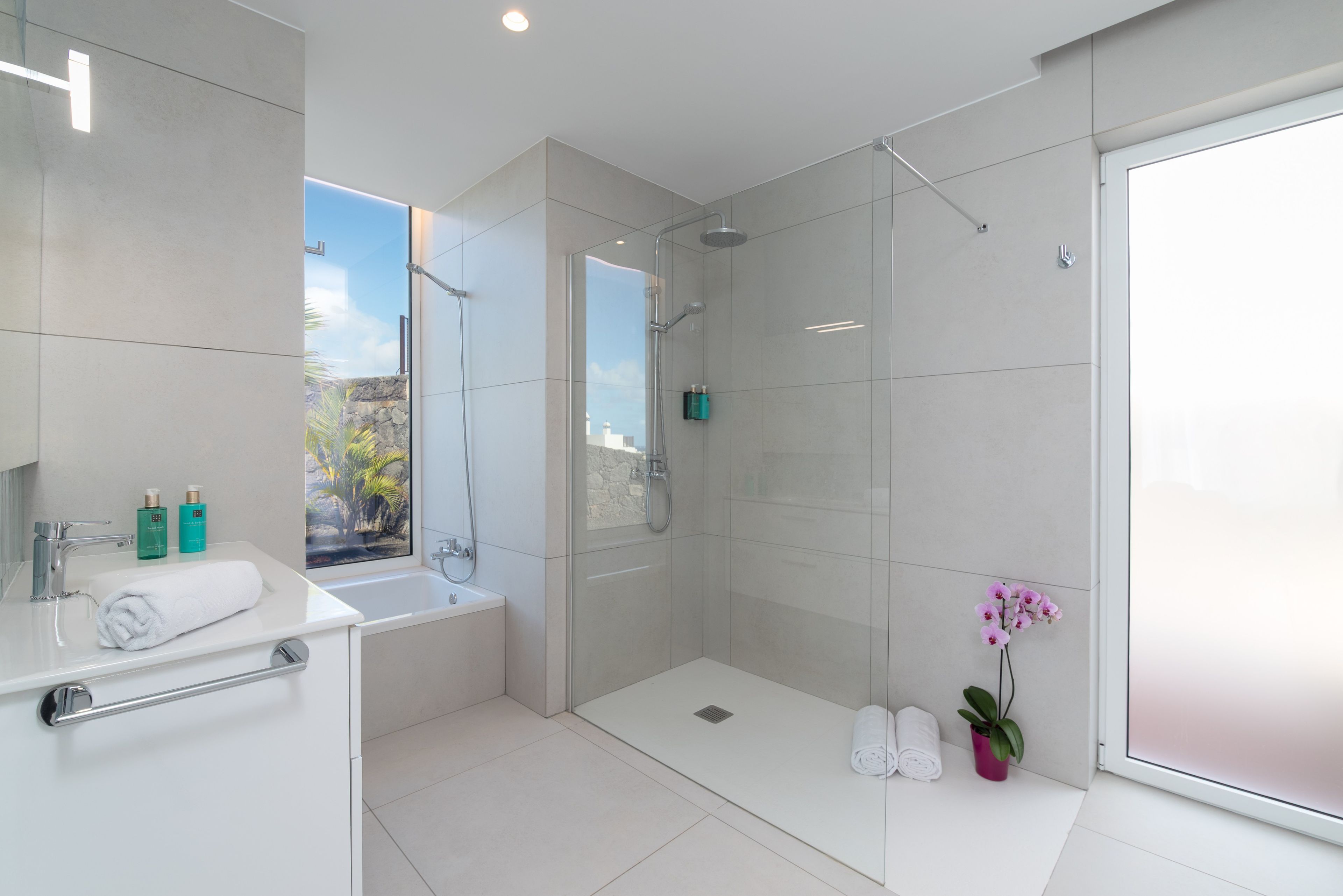 A modern bathroom with a glass shower enclosure, a bathtub, and a sink with a towel.