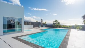 Une piscine extérieure moderne, avec une eau d’un bleu limpide, entourée d’une terrasse carrelée de blanc et d’un mur en pierre.