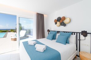 Quarto de hotel com cama, vista para o mar e varanda com espreguiçadeiras.