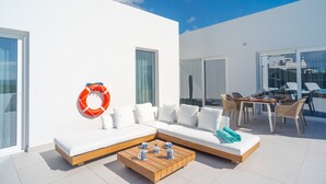 Un espace de vie extérieur moderne, avec un canapé blanc, une table basse en bois et un ensemble de mobilier de salle à manger.