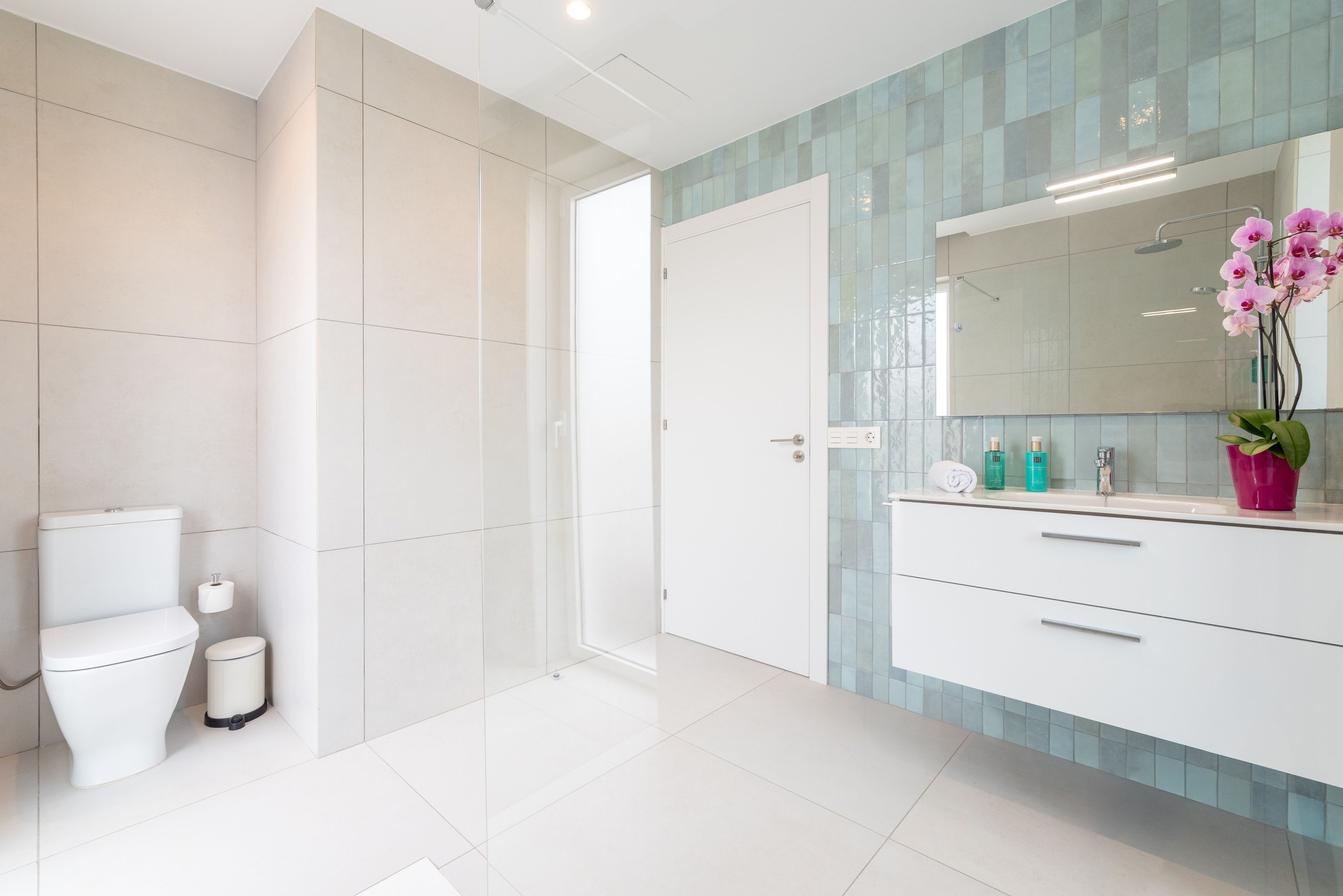 A modern bathroom with a toilet, a bidet, a shower, and a vanity with a mirror.