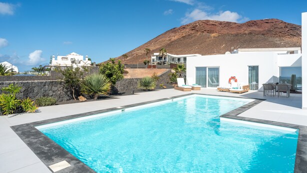Une piscine avec une chaîne de montagnes en arrière-plan, des bâtiments blancs et un ciel dégagé.
