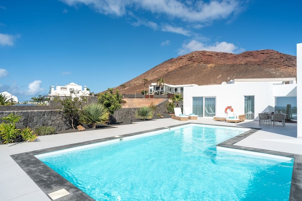 Piscina com montanhas ao fundo, edifícios brancos e céu claro.