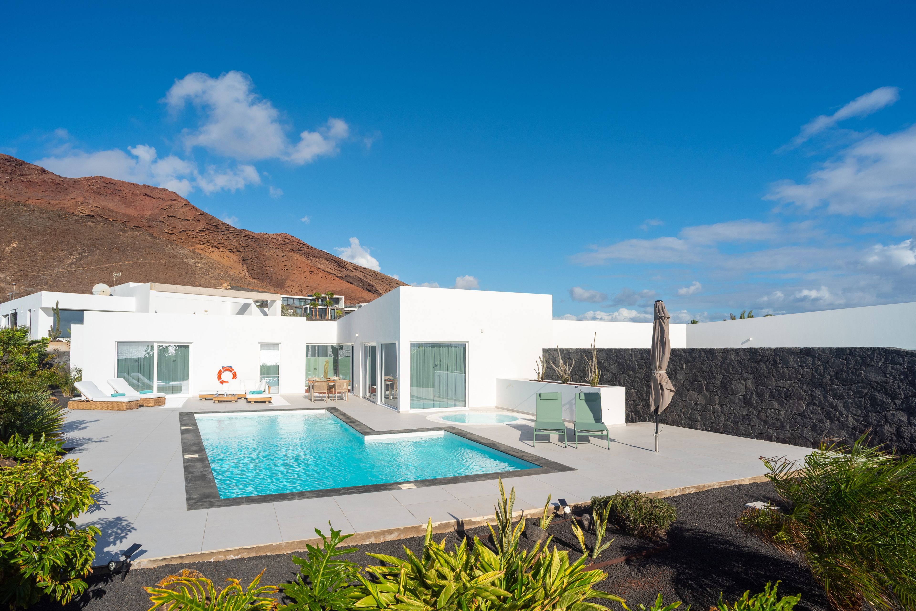 A modern house with a swimming pool, a dining area, and a view of a mountain.