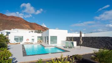 A modern house with a swimming pool, a dining area, and a view of a mountain.